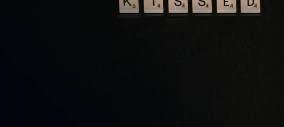 immagine grafica con sfondo nero e in alto lettere del gioco scarabeo che compongono la parola KISSED