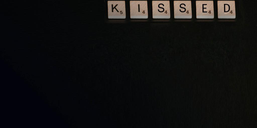 immagine grafica con sfondo nero e in alto lettere del gioco scarabeo che compongono la parola KISSED